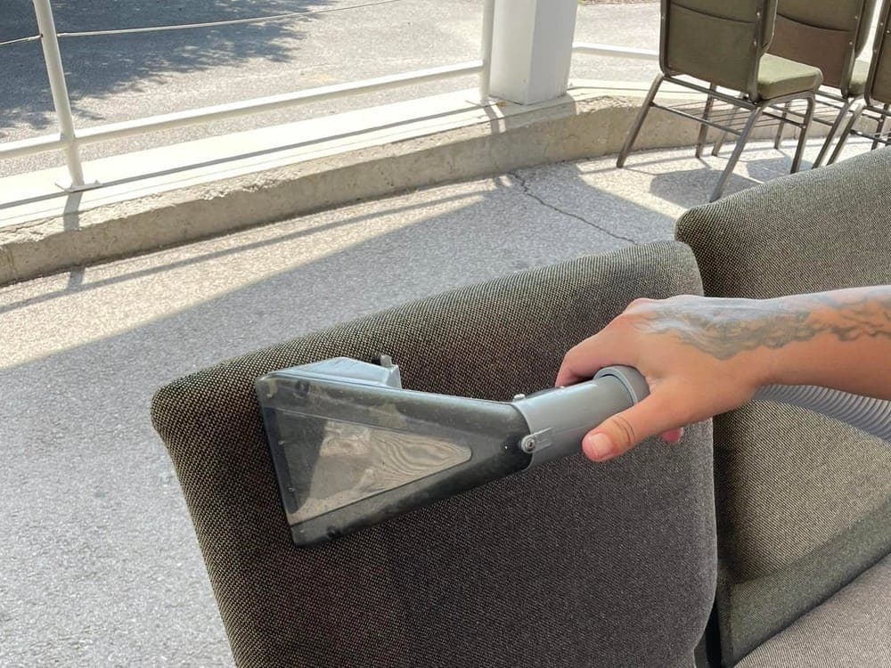 An upholstered chair being cleaned with an extraction tool.